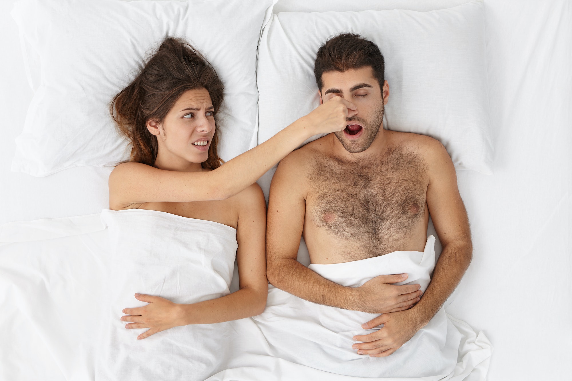 Frustrated and nervous woman lies near snore man, being unable to sleep, tries to stop loud sounds,